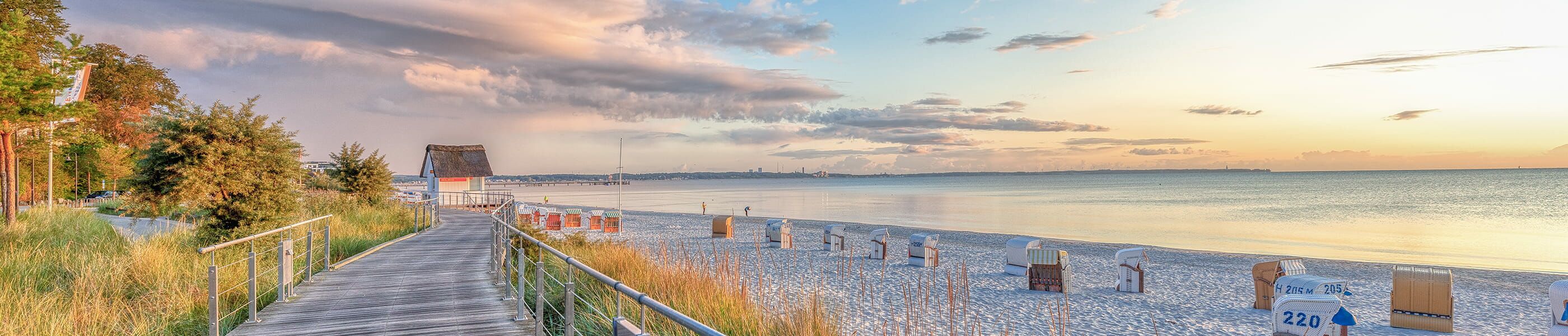 Scharbeutz Strandpromenade bei Sonnenuntergang mit Strandkörben, Holzsteg und ruhiger Ostsee in warmem Licht.