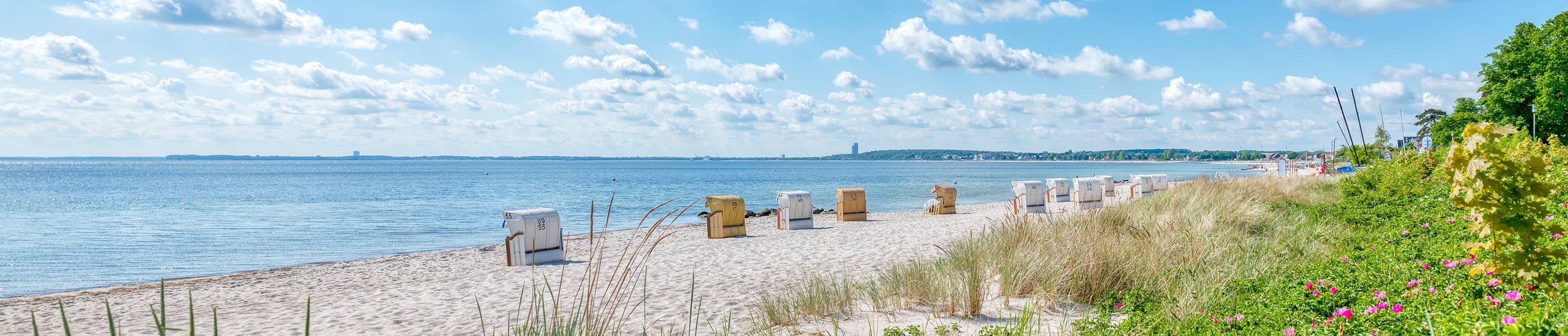 Sandstrand in Sierksdorf mit Strandkörben, Dünen und Ostseepanorama bei klarem Himmel und sanften Wellen.